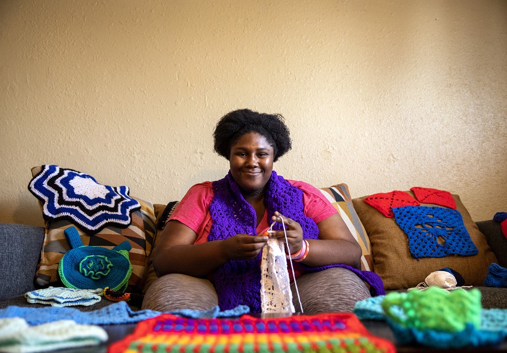 Precious sits with a collection of her yarn creations. She was in the beginning stages of working on a blanket when visited. [Credit: Nathan Poppe]