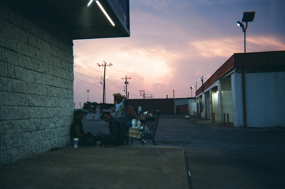 The sunset looms behind three people sitting outside the Ontrac Convenient Store in South OKC. Mark said he crouched to take the photo because he wanted to get a perspective from where his subjects were sitting. 