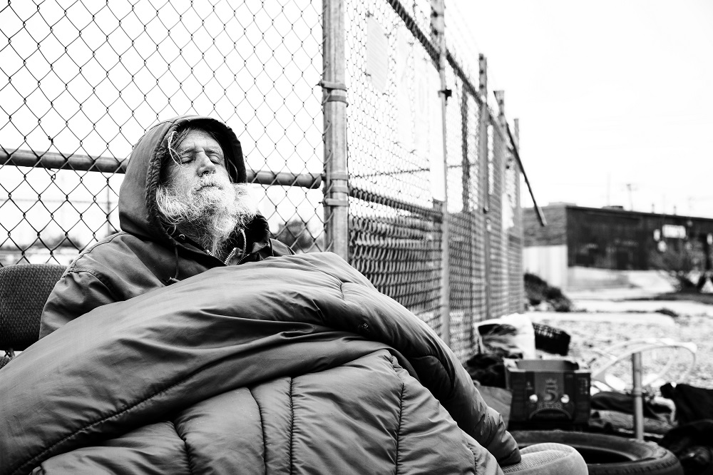 Jim kept warm under a sleeping bag on a freezing cold April 2 morning. He rarely leaves his camp and has been struggling with not being able to secure a bed at night. [Credit: Nathan Poppe]