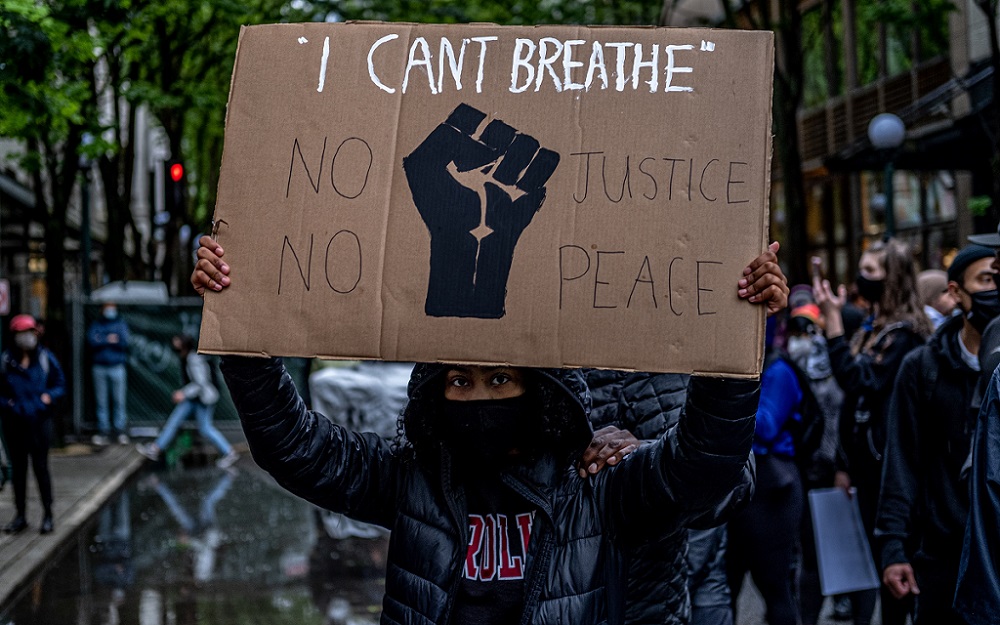 A Seattle protester holds a sign quoting the last words of both George Floyd and Eric Garner — Black men who were killed by white police officers, Floyd in Minneapolis and Garner in New York. 30 May. [Credit: Mark White/Real Change]