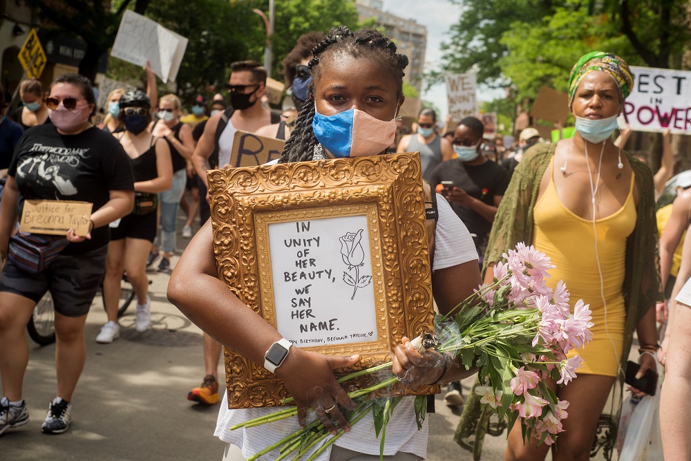 A protester holds a memorial sign for Breonna Taylor, which reads "In unity of her beauty, we say her name." [Credit: Kathleen Hinkel/StreetWise]
