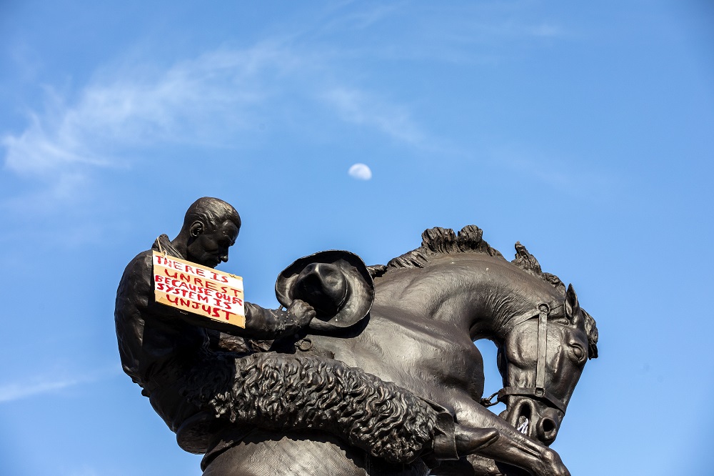 A sign hangs around the neck of a statue at the Oklahoma State Capitol building on May 31, 2020. Photo by Nathan Poppe, The Curbside Chronicle.