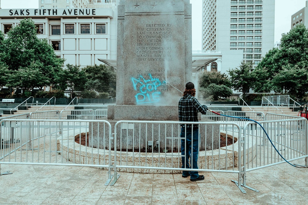 A man with a power washer removes anti-police graffiti from Union Square’s Dewey Monument. [Credit: Kit Castagne]