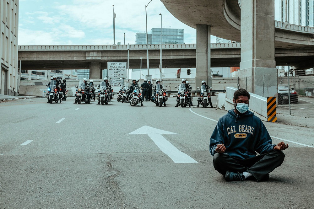 A protester sits in front of police assigned to keep protesters from marching onto the Bay Bridge. [Credit: Kit Castagne]