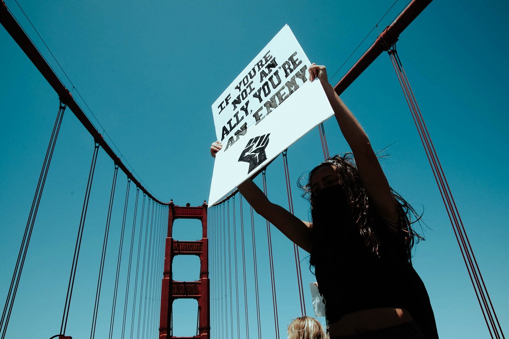 A protester holds a sign while standing on the Golden Gate Bridge’s median strip. [Credit: Kit Castagne]