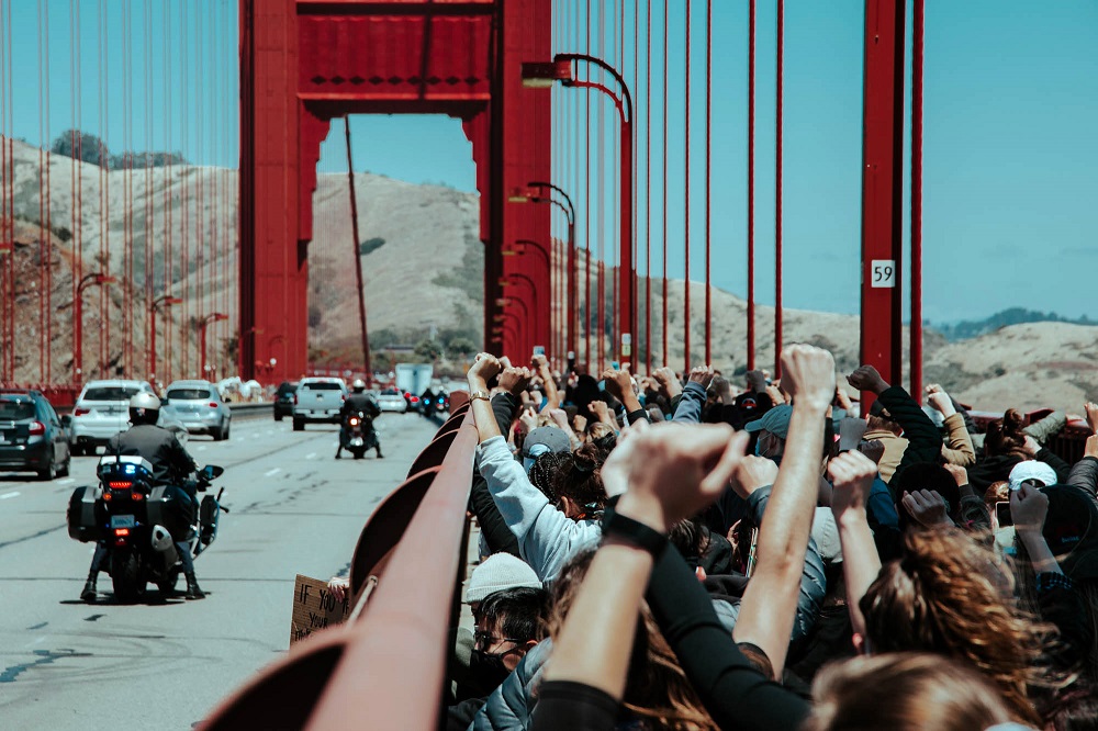 Protesters kneel together and raise their fists on the Golden Gate Bridge. [Credit: Kit Castagne]