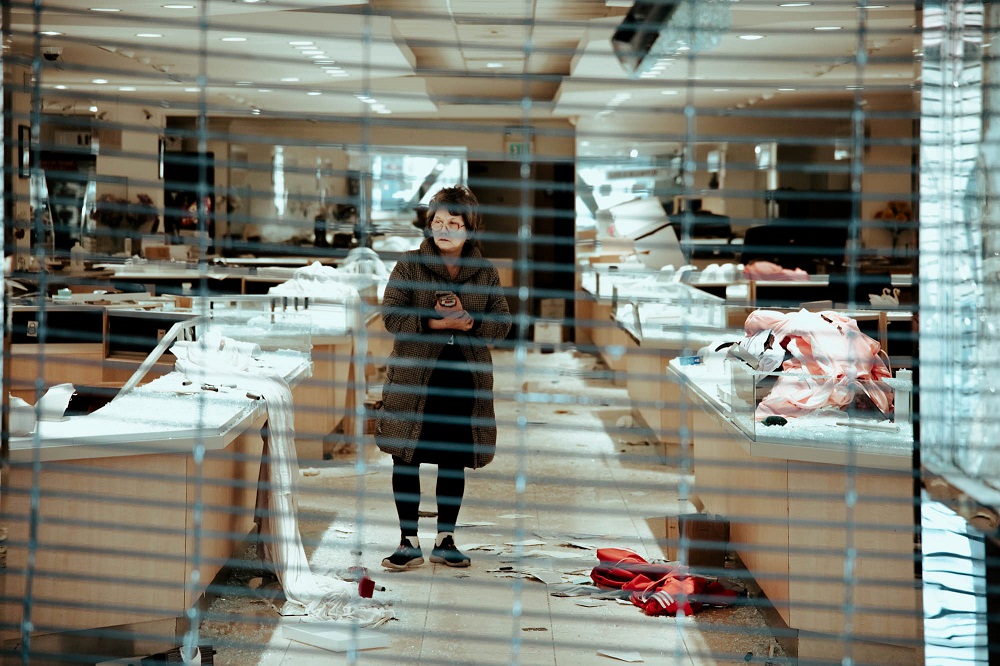 A woman surveys the damage to Grace Jewelers on O’Farrell Street after looters had torn through the metal gates and robbed the store the night before. [Credit: Kit Castagne]