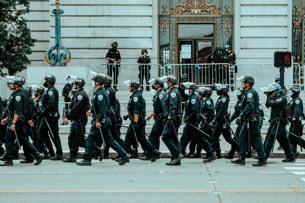 Police officers trail a protest marching away from City Hall. [Credit: Kit Castagne]