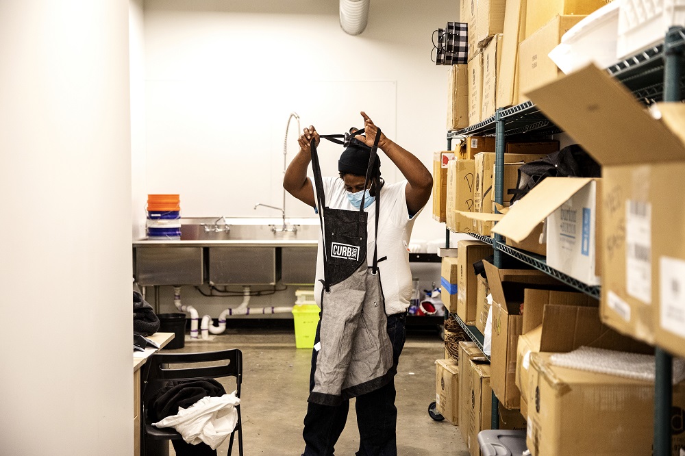 Corey ties his Curbside Flowers apron in the shop’s backroom. [Credit: Nathan Poppe, The Curbside Chronicle]