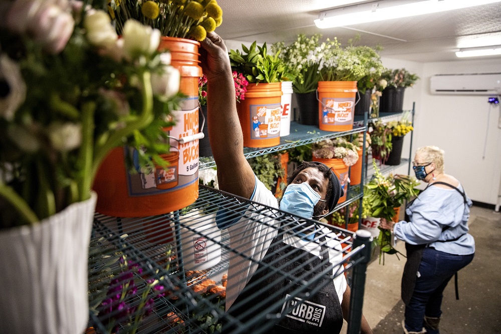 Corey reaches for a flower in the Curbside Flowers cooler. [Credit: Nathan Poppe, The Curbside Chronicle]