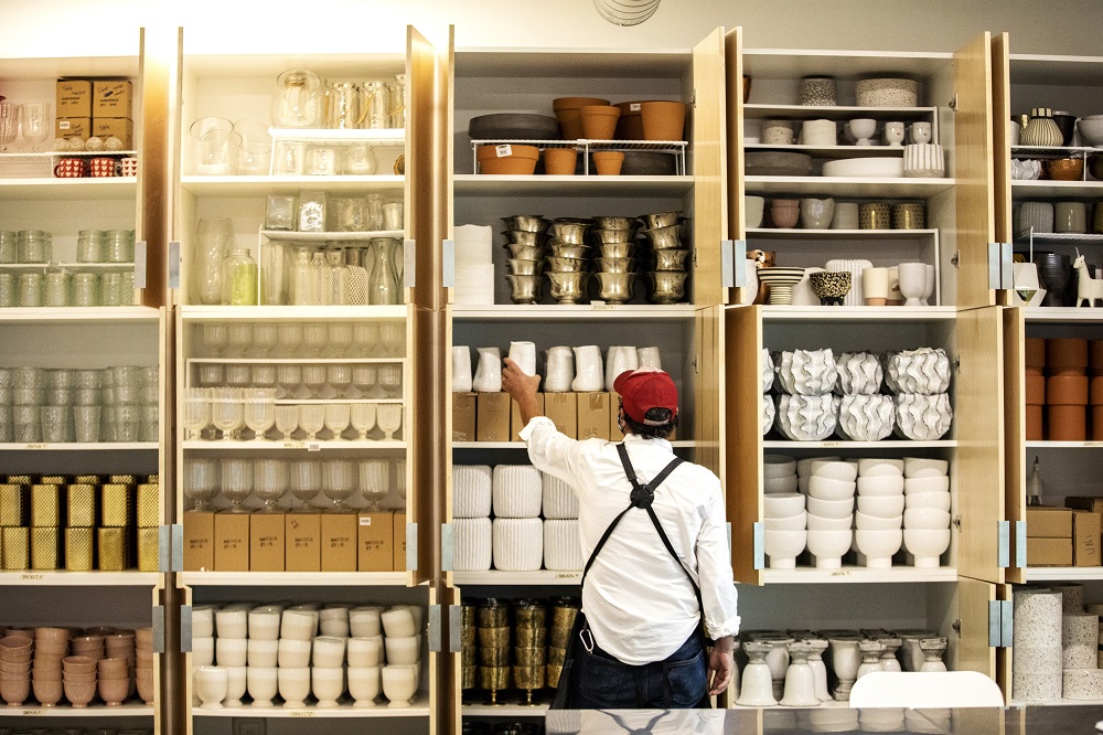 Gary reaches for a vase from a wall of cabinets lining the back of Curbside Flowers. [Credit: Nathan Poppe, The Curbside Chronicle]